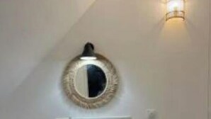 Ein Badezimmer mit rundem Spiegel, Waschbecken in Weiß, dunklem Schminktisch und einer Wandleuchte.