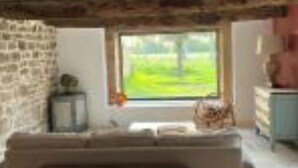 Ein rustikaler Raum mit freiliegenden Holzbalken, einer Steinwand, einem großen Fenster mit Blick auf Grünflächen, einer Couch und einer Kommode.
