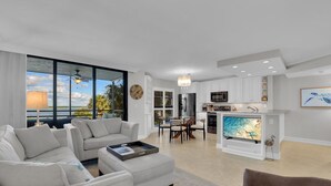 A modern living room with a large TV, a dining area, and a kitchen. - Waterfront in Old Marco!  Beautiful unit!  Deluxe! (Marco Island)