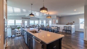 A modern kitchen with a large island, pendant lighting, and a view of the ocean.