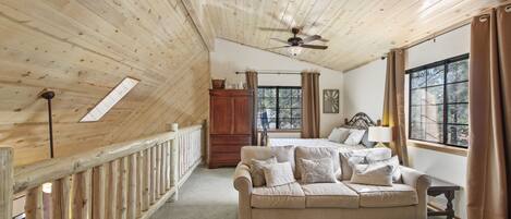 A cozy room with a wooden ceiling, a sofa, a coffee table, and a window with curtains.