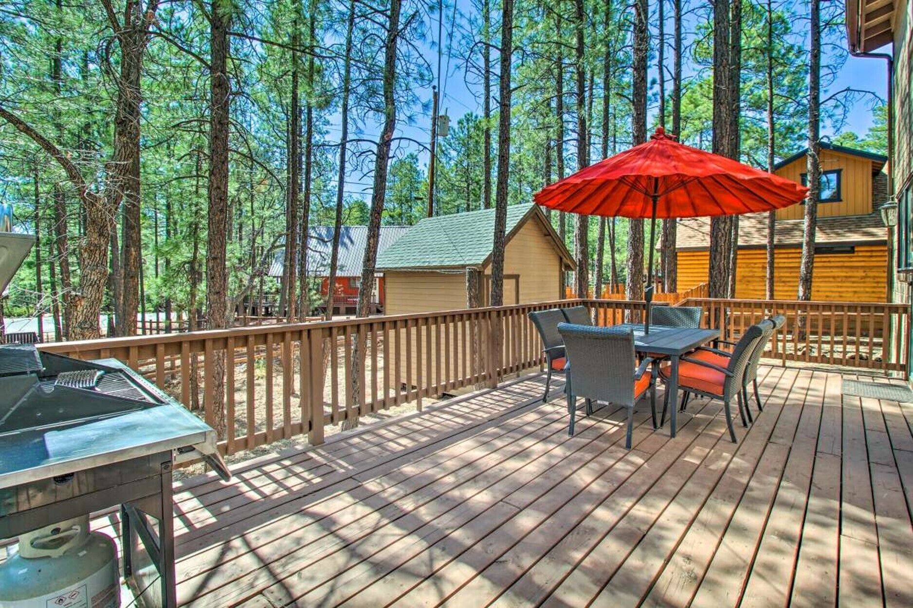 A deck with a table and chairs, a red umbrella, and a grill.