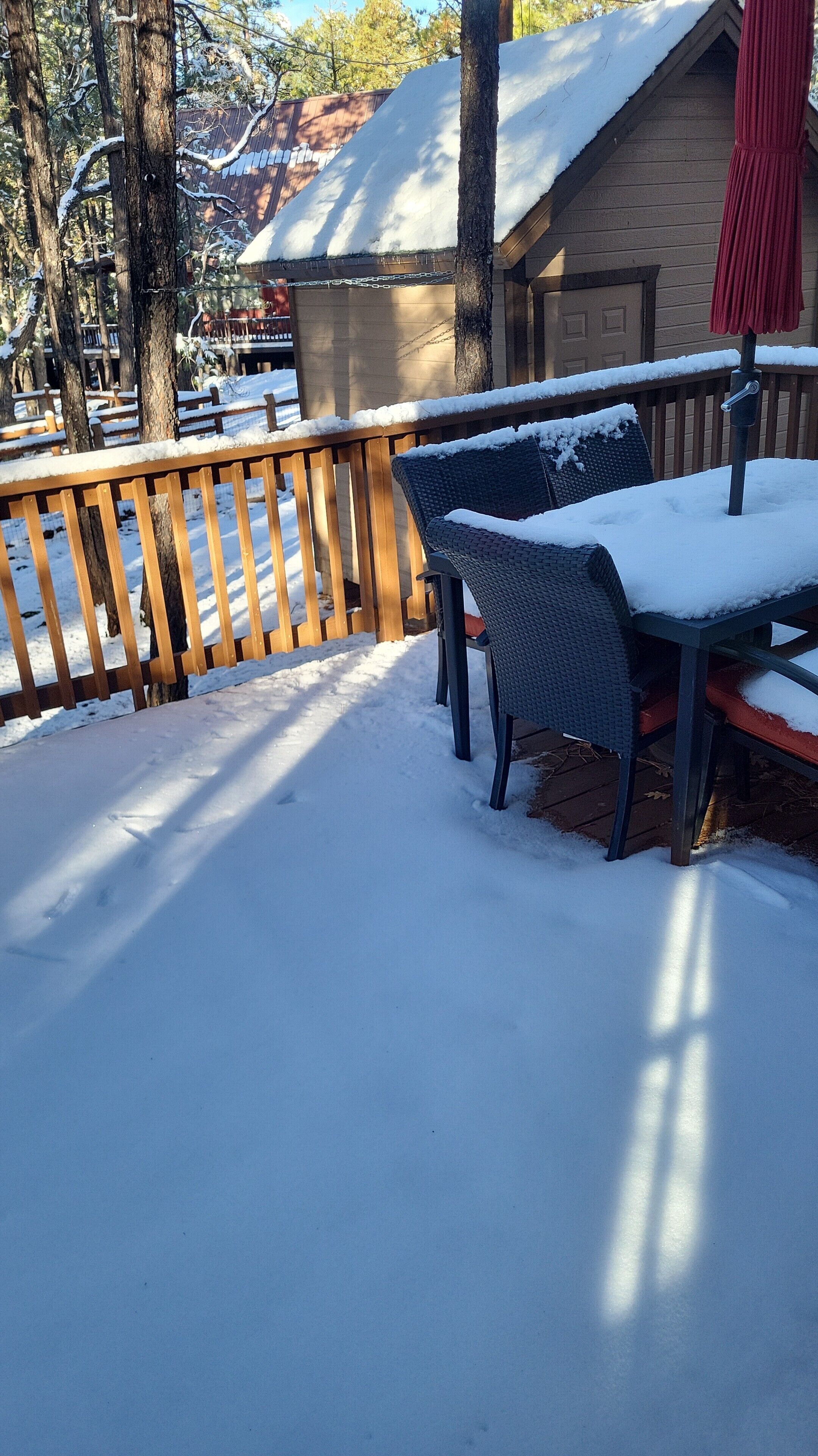 A wooden deck with a metal railing, a covered outdoor seating area, and a building with a snow-covered roof.