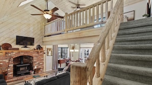 A spacious living area with a fireplace, a wooden staircase, and a balcony with a railing. - Tranquil Pinetop Getaway! w/Firepit, Grill, Deck, Pet-Friendly, Near Ski & Golf! (Pinetop)