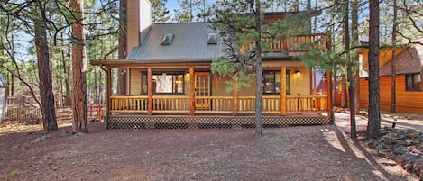 A cabin with a wooden deck, surrounded by tall pine trees.