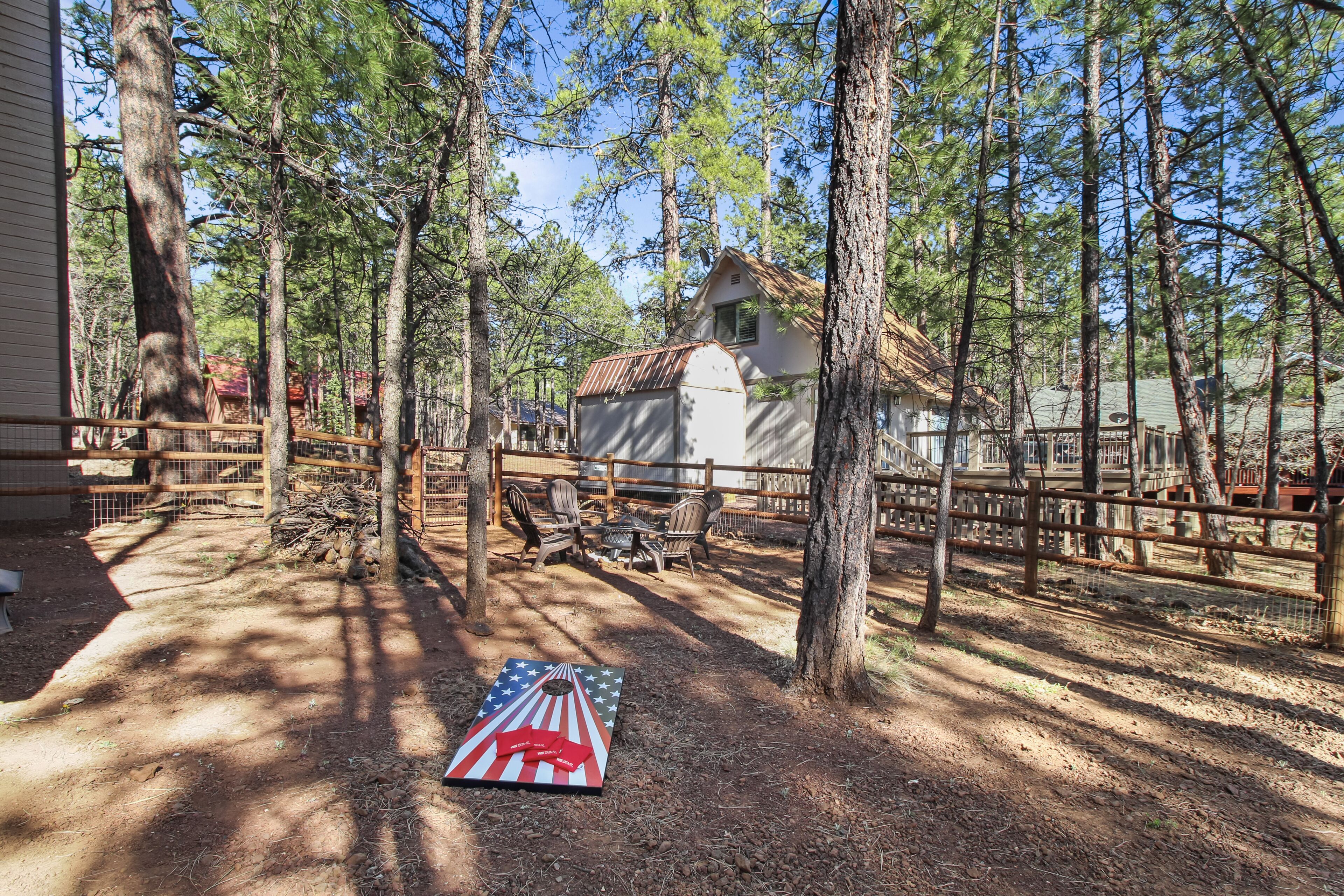 A rustic cabin surrounded by tall trees, a wooden fence, and a picnic table.