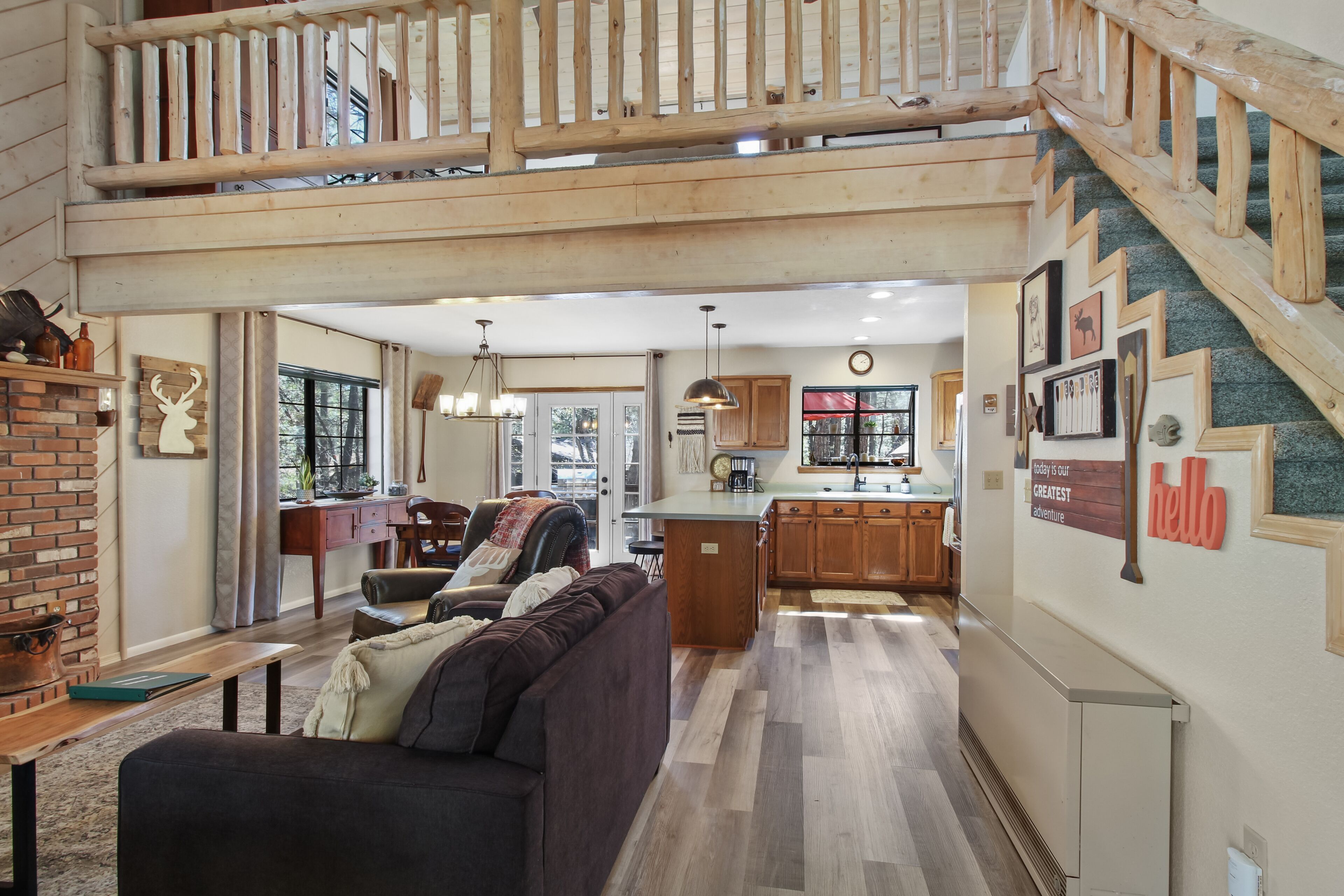 A spacious living area with a dark brown sofa, a wooden bench, and a brick fireplace. A kitchen with wooden cabinets and a large island is visible in the background.