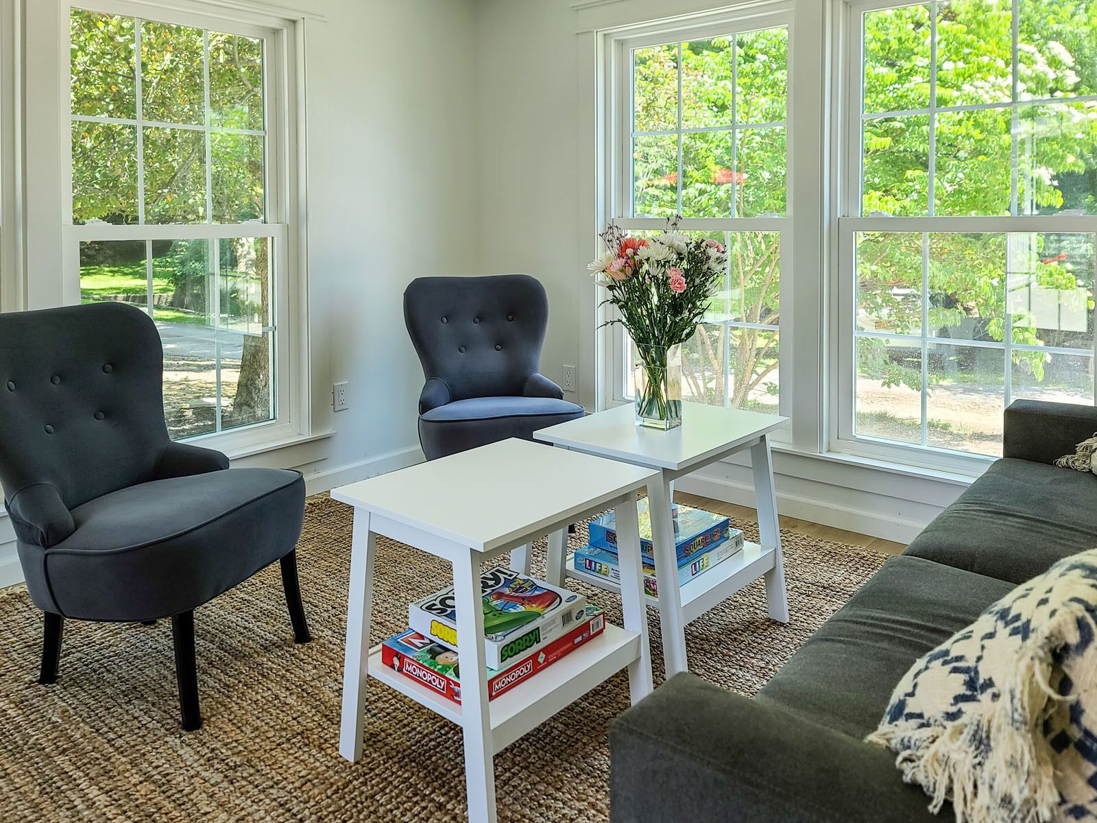 A living room with two black armchairs, a white coffee table with board games, and a vase of flowers.