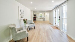 A spacious living area with a kitchen in the background, wooden flooring, and large windows. - Fun Getaway Lakehouse in the Hudson Valley (Craryville)