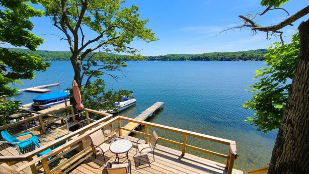 A wooden deck with outdoor seating, overlooking a calm lake with boats docked nearby. - Fun Getaway Lakehouse in the Hudson Valley (Craryville)