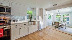 A modern kitchen with white cabinetry, a stainless steel sink, and a dining area with a wooden table and chairs. - Fun Getaway Lakehouse in the Hudson Valley (Craryville)