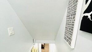 A narrow staircase with a wooden handrail, white walls, and a carpeted landing area. - Main Central Avenue Basement Studio (Saskatoon)