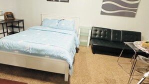 A bedroom with a bed, a black sofa, a small table with a vase, and a framed picture on the wall. - Main Central Avenue Basement Studio (Saskatoon)