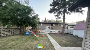 A residential backyard with a playset, a swing, and a basketball hoop. - Main Central Avenue Basement Studio (Saskatoon)