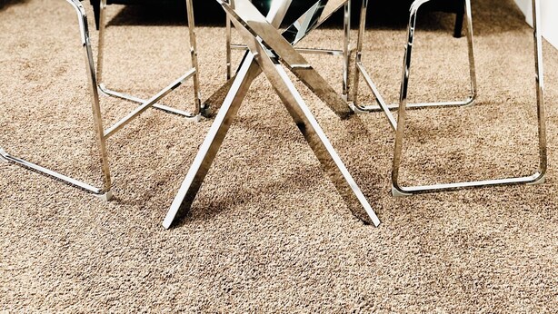 A round glass table with a white candle, metal legs, and a decorative item on a carpeted floor. - Main Central Avenue Basement Studio (Saskatoon)