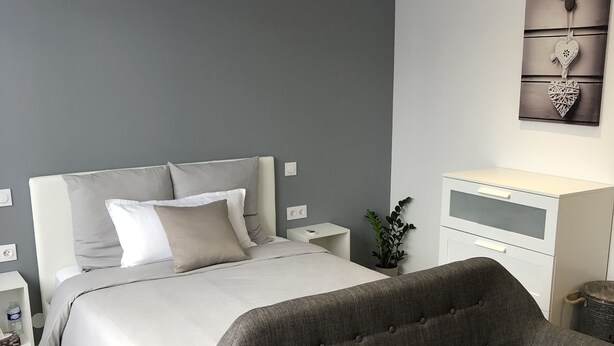 A modern bedroom with a bed, bedside tables, a grey upholstered armchair, a white dresser, and a wall-mounted artwork. - The Green cocoon: Above the Alsatian vineyard (Turckheim)