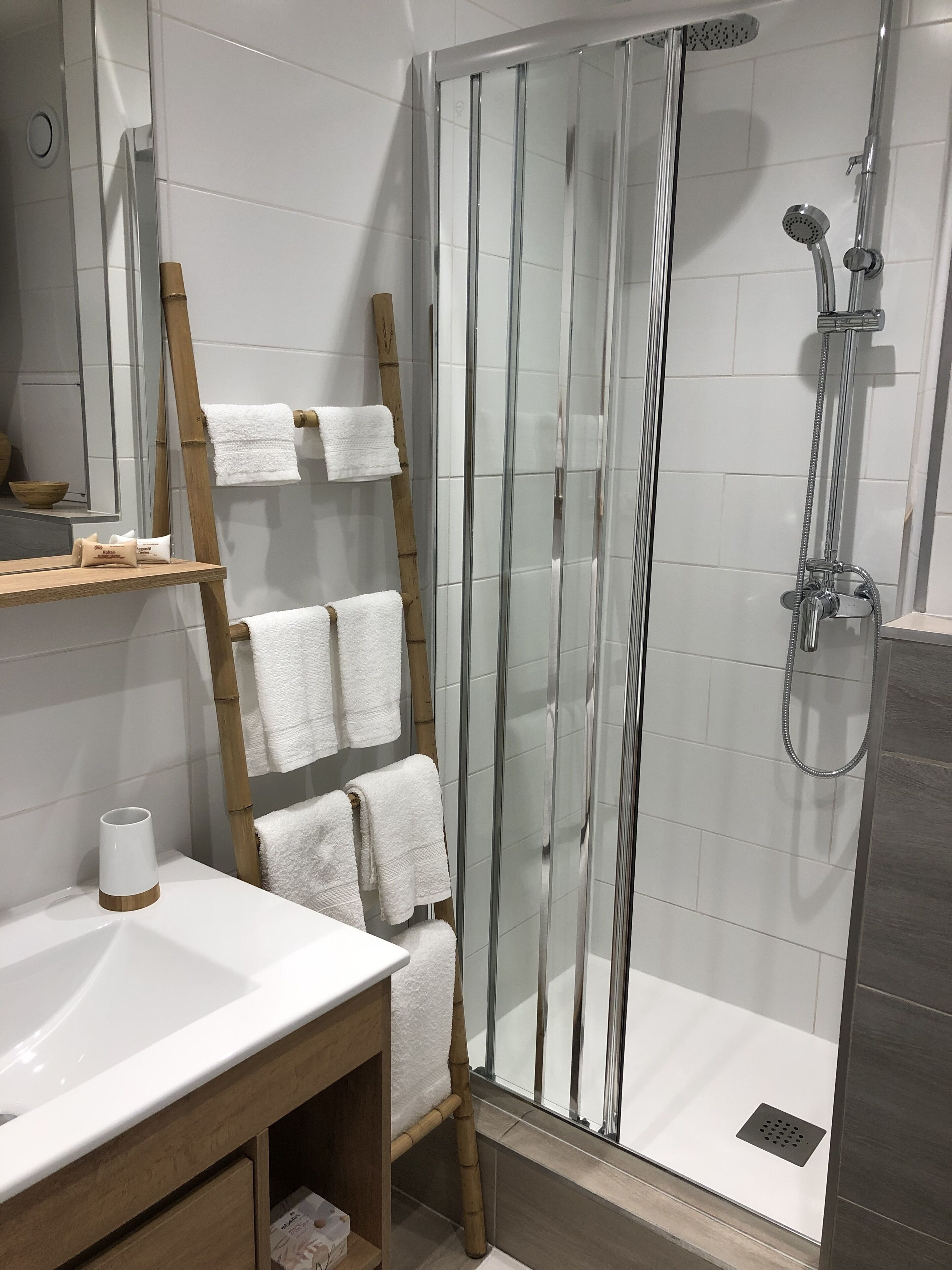 A modern bathroom with a glass-enclosed shower, a wooden towel rack, a white sink, and a mirror.