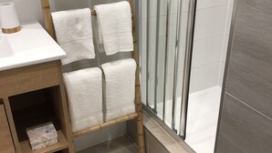 A bathroom with a wooden towel rack holding six white towels, a wooden vanity with a white countertop, and a glass shower enclosure. - The Green cocoon: Above the Alsatian vineyard (Turckheim)