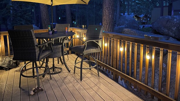 An outdoor deck with a round table and chairs, an umbrella, and string lights.