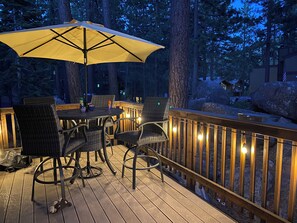 Eine Terrasse im Freien mit einem runden Tisch, Stühlen, einem Sonnenschirm und Lichterketten.
