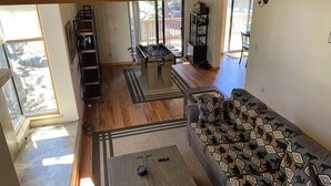 A living room with a sofa, coffee table, and foosball table. There is a staircase leading to a deck with a railing.