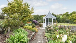 Een tuin met een prieel, een pad van stenen en verschillende planten.
