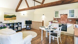 Een ruime woonkamer met een houten plafond, een eettafel met stoelen, een boekenkast en een televisie.