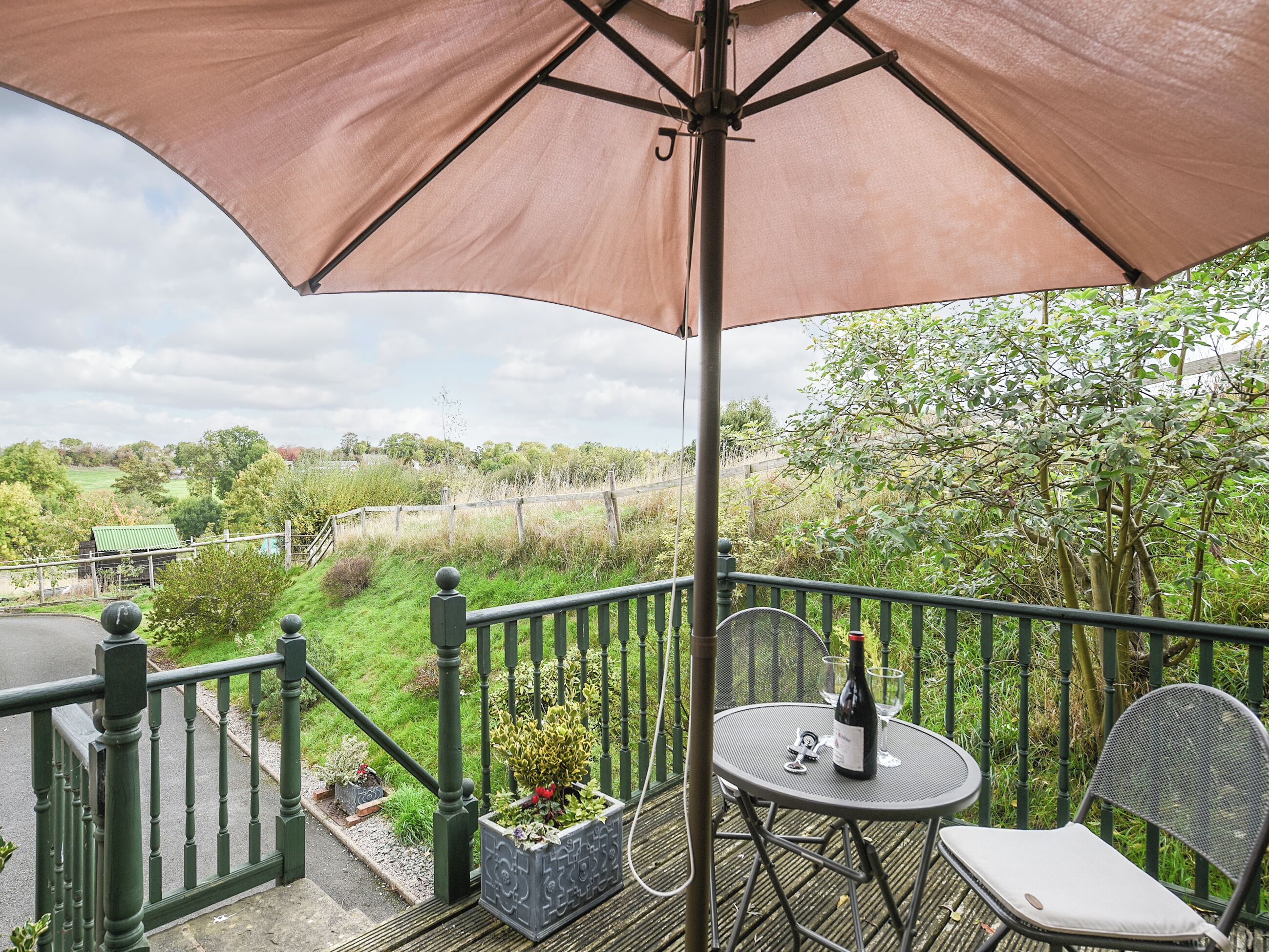 A balcony with a table and chairs, a bottle of wine, and a large umbrella.