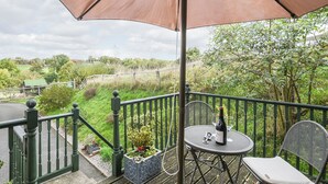 Een balkon met een tafel en stoelen, een fles wijn en een grote parasol.