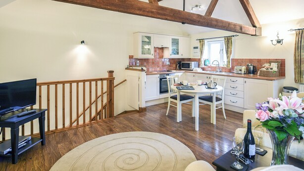 Een ruime woonkamer met een houten trap, een eettafel met stoelen, een televisie en een keuken met moderne apparatuur.