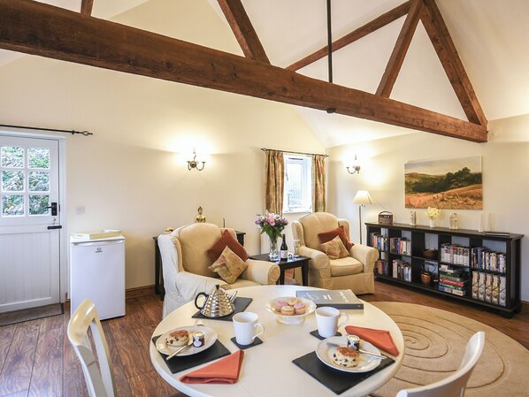 A cozy room with a dining table set for a meal, two armchairs, a bookshelf, and a window with curtains.