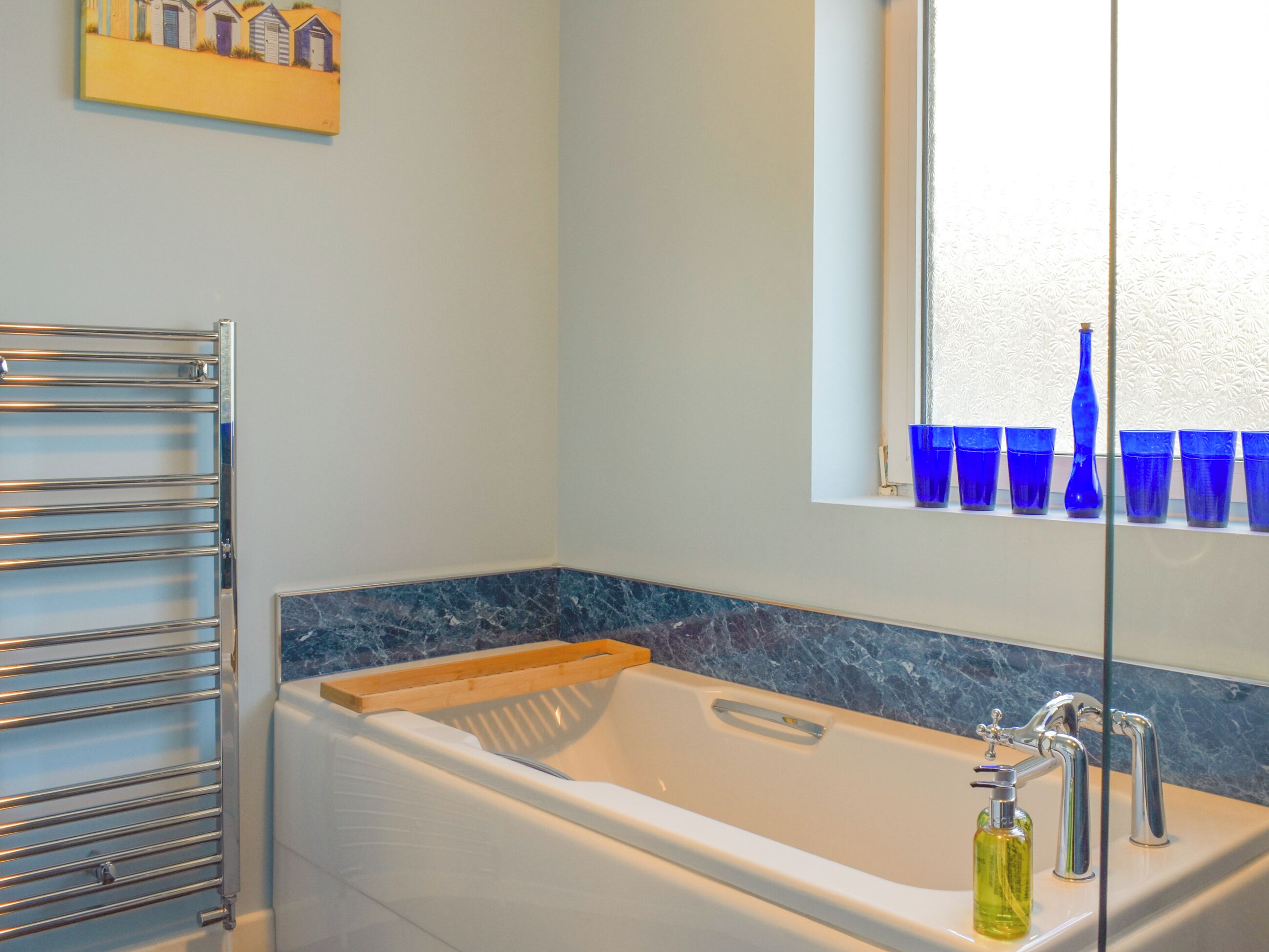 Une salle de bain avec une baignoire, une fenêtre avec des vitres bleues et un porte-serviettes.