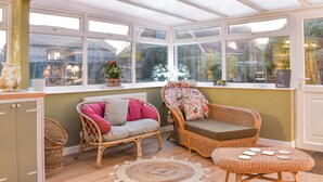 A conservatory with wicker furniture, a woven floor mat, and a view of the outside.