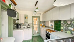 A kitchen with white cabinets, a green tiled backsplash, a wooden countertop, and a stainless steel sink.