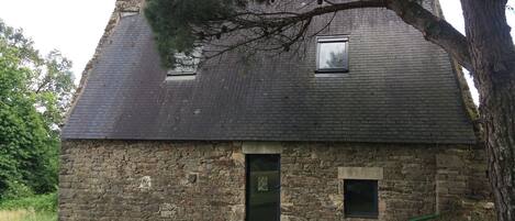 A stone house with a steep roof, two windows, and a door.