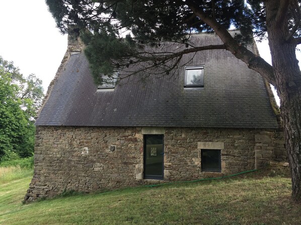A stone house with a steep roof, two windows, and a door.