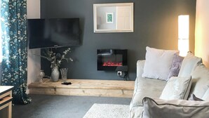 A living room with a flat-screen TV, a fireplace, a sofa, and a window with curtains. - 2 bedroom accommodation in Girvan (Girvan)