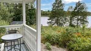 A covered porch with a table and chairs, overlooking a lake with trees and shrubs. - Cozy home in Harmånger with lake view (Harmånger)