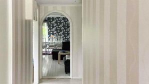 A hallway leading to a dining area with a black floral wallpaper, white chairs, and a table with a vase of flowers. - Cozy home in Harmånger with lake view (Harmånger)