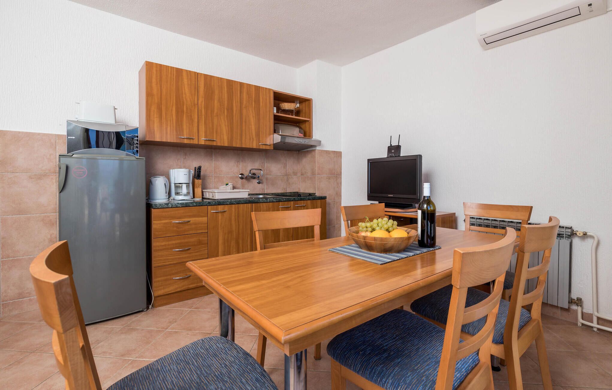 A compact kitchen with wooden cabinets, a built-in oven, a coffee maker, and a television.