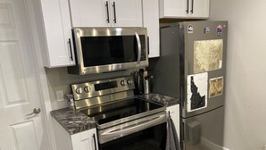 A kitchen with white cabinets, a stainless steel microwave, oven, and refrigerator, and a granite countertop.