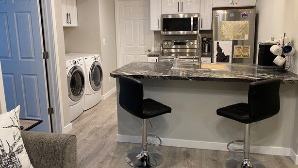 A modern kitchen with a marble countertop, stainless steel appliances, and two black bar stools.