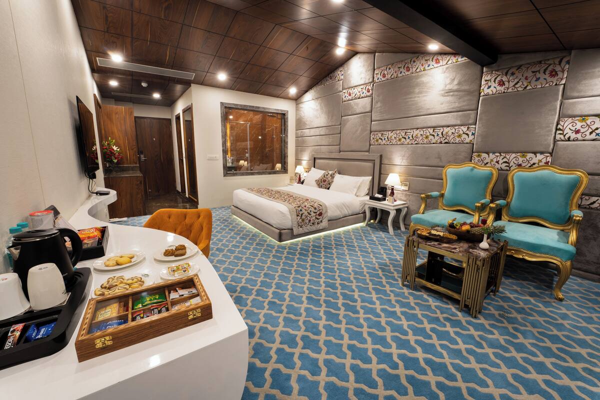 A hotel room with a bed, a seating area with chairs, a coffee station, and a decorative wall.