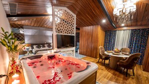 A spa room with a hot tub, wooden flooring, a chandelier, and a dining area with a table and chairs. - Hotel Snowland Srinagar (Srinagar)