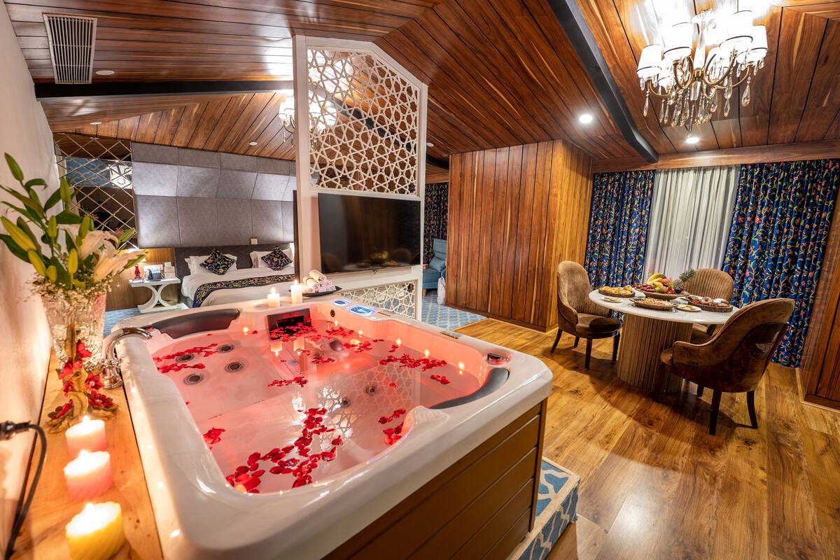 A spa room with a hot tub, wooden flooring, a chandelier, and a dining area with a table and chairs.