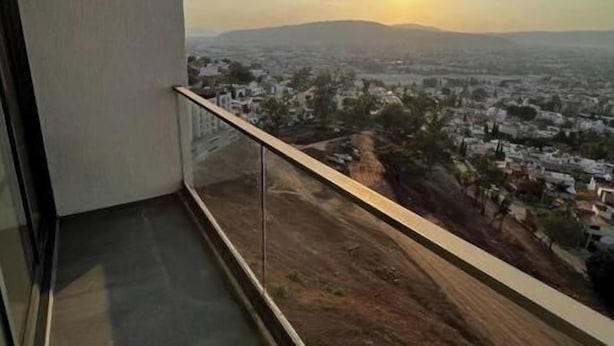 Un balcon offrant une vue dégagée sur le paysage urbain et sur le soleil se couchant à l’horizon.