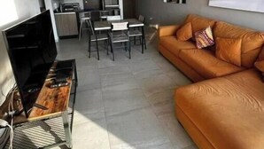 Un salon moderne comprenant un canapé, un téléviseur et un coin repas avec des chaises et une table.