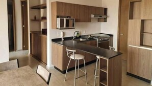 Une cuisine moderne avec des armoires en bois, un comptoir noir, un four à micro-ondes encastré, une cuisinière et deux tabourets de bar.