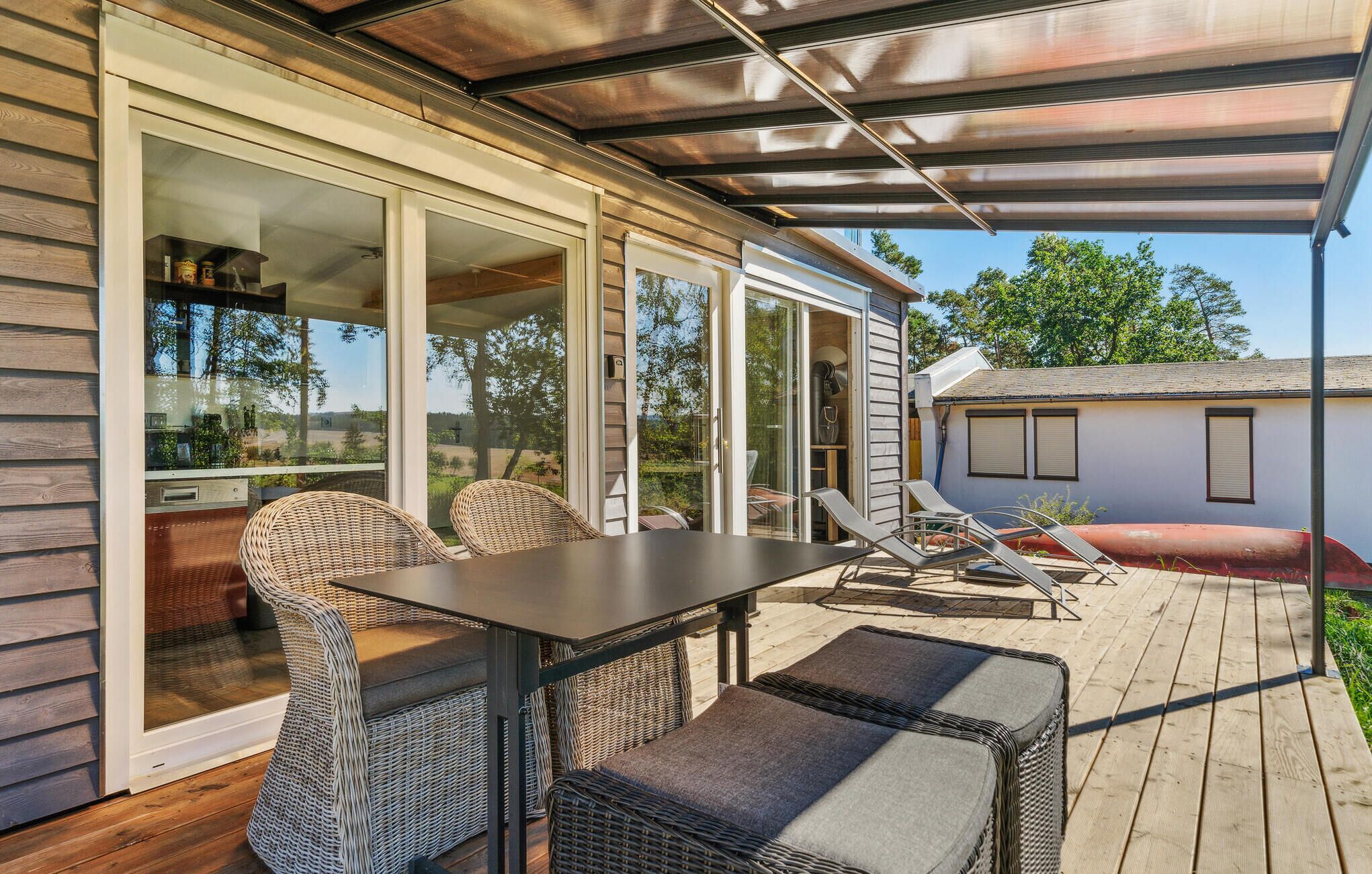 Une terrasse couverte, aménagée avec des meubles en osier, une table et offrant une vue sur les environs.