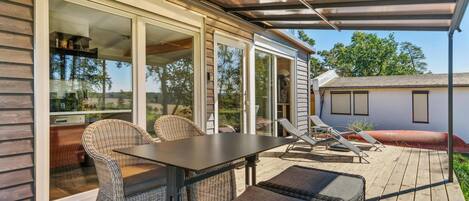 Une terrasse couverte, aménagée avec des meubles en osier, une table et offrant une vue sur les environs.